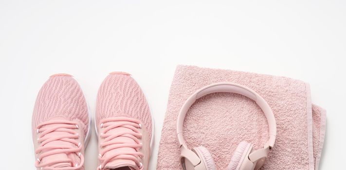 pair of pink textile sneakers, wireless headphones and a textile pink towel on a white background. Set for sports, running