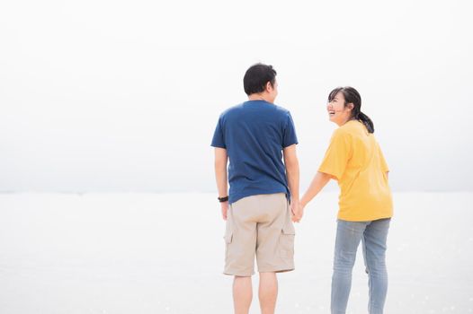 Asian couples holding hands together on a private beach by the sea background. Happy man and woman laughing together on travel vacation. Love affection and Valentines day concept. Copy space