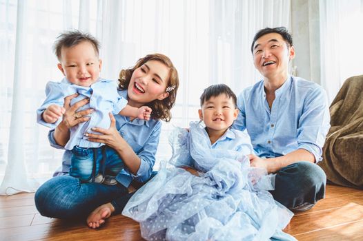 Happy Asian family smile and laugh together in living room at home. Two parents and two children kids. People lifestyle in state quarantine after travel on Covid-19 or Coronavirus epidemic concept