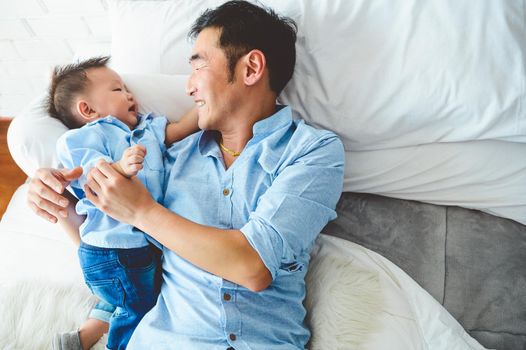 Asian father and son playing together on white bed in bedroom in the morning. Two people having leisure time at home. People lifestyle concept.