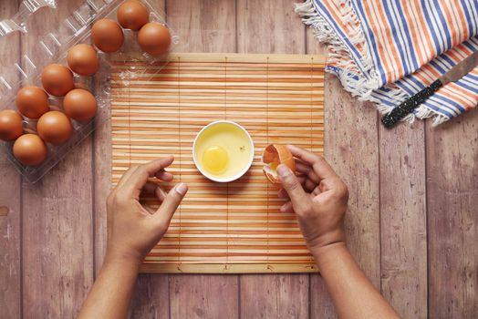 man breaking egg and pouring into a small container on table