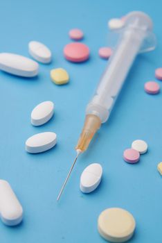 syringe and pills on blue background, close up .