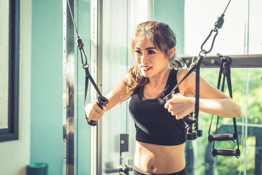 Asian young woman doing elastic rope exercises at cross fitness gym. Strength training and muscular Beauty and Healthy concept. Sport equipment and Sport club center theme. 