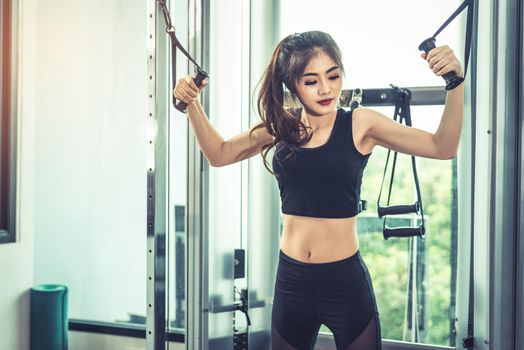 Asian young woman doing elastic rope exercises at cross fitness gym. Strength training and muscular. Beauty and Healthy concept. Sport equipment and Sport club center theme. 