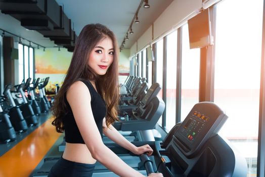 Asian sport woman walking or running on treadmill equipment in fitness workout gym. Sport and Beauty concept. Workout and Strength Training theme. Cardio and Diet theme