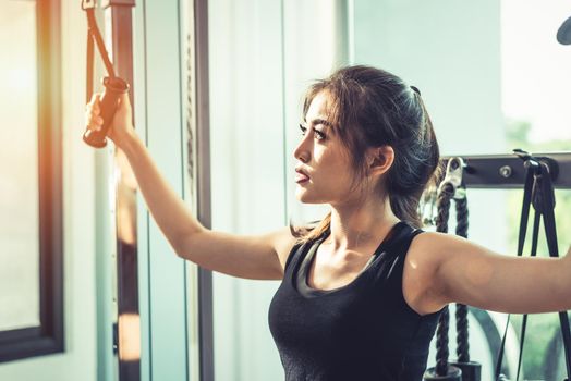 Asian young woman doing elastic rope exercises at cross fitness gym. Strength training and muscular. Beauty and Healthy concept. Sport equipment and Sport club center theme. 