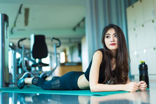 Sports woman lying and relaxing on yoga mat in fitness gym with sports equipment background. Beauty and Workout training exercise concept. Body build up and Strength theme.