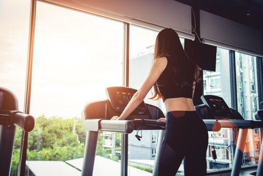 Asian sport woman walking or running on treadmill equipment in fitness workout gym. Sport and Beauty concept. Workout and Strength Training theme. Cardio and Diet theme