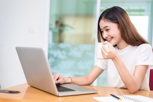 Asian woman enjoy herself while using laptops and internet in office. Business and marketing and part time concept. On line shopping and business success theme. Happy mood doing working job.