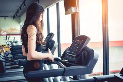 Asian woman using smart phone when workout or strength training at fitness gym on treadmill. Relax and Technology concept. Sports Exercise and Health care theme. Happy and Comfortable mood.