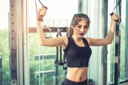 Asian young woman doing elastic rope exercises at cross fitness gym. Strength training and muscular Beauty and Healthy concept. Sport equipment and Sport club center theme. 
