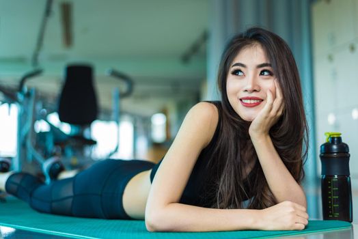 Sports woman lying and relaxing on yoga mat in fitness gym with sports equipment background. Beauty and Workout training exercise concept. Body build up and Strength theme.