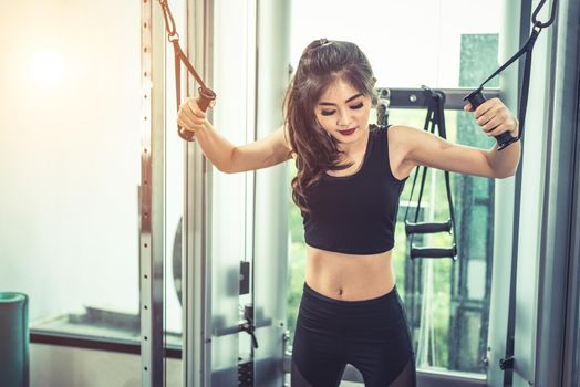 Asian young woman doing elastic rope exercises at cross fitness gym. Strength training and muscular. Beauty and Healthy concept. Sport equipment and Sport club center theme. 