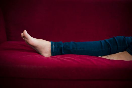 Woman legs with wearing jeans while relaxing at movie theater or home at the red sofa, Relax and holiday concept, Bed time sleeping concept