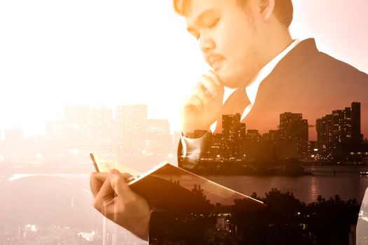 Businessman looking memo and Thinking for idea with big city or town in background,Double exposure, panoramic view contemporary megalopolis background, orange sun light, business concept