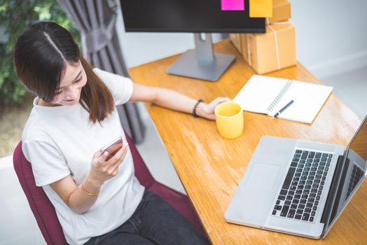 Top view of woman using mobile phone and laptop as shopping buyer by internet technology in office. Business entrepreneur checking her customer order in stock and sending product by drop shipping