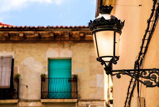 Old house facade with rusty balcony and blind next to vintage streetlight. Novelda village, Valencia community, Spain.