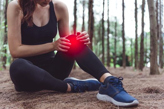 Sport woman injury at knee during jogging in forest. Pine woods background.  Medical and Healthcare concept. Nature and People theme. Lifestyles theme. Red light spot use