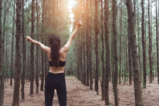Woman stretching arms and breathing fresh air in middle of pinewood forest while exercising. Workouts and Lifestyles concept. Happy life and Healthcare theme. Nature and Outdoors theme. Back view