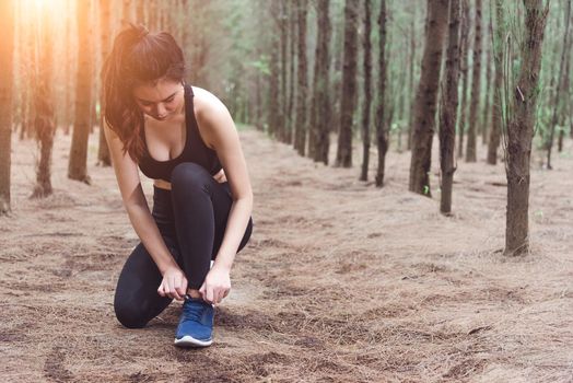 Woman tying up shoelaces when jogging in forest back with drinking water bottle beside hers. Sneakers rope tying. People and lifestyles concept. Healthcare and Wellness theme. Park and Outdoors theme.