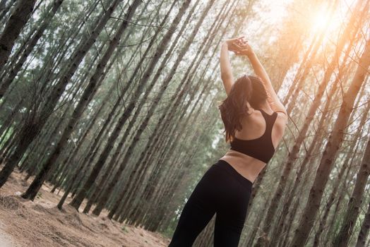 Women stretching arms and breathing fresh air in middle of pinewood forest while exercising. Workouts and Lifestyles concept. Happy life and Healthcare theme. Nature and Outdoors theme. Back view