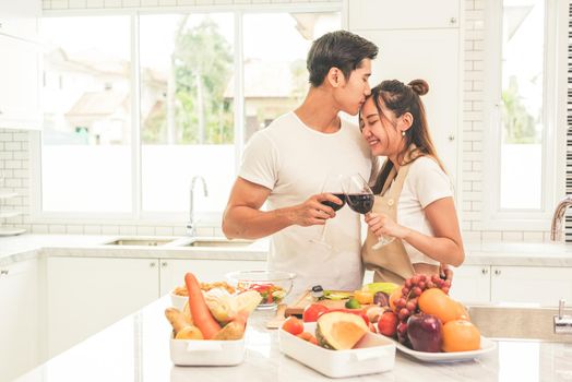 Asian lovers or couples kissing forehead and drinking wine in kitchen room at home. Love and happiness concept Sweet honeymoon and Valentine day theme