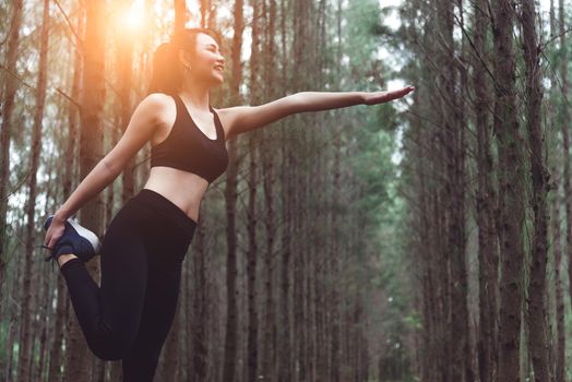 Beauty Asian woman doing yoga and stretching legs before running in forest at outdoors. Sports and Nature concept. Lifestyle and Activity concept. Pine woods theme.