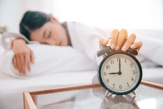 Asian young beauty woman turning off alarm clock in Morning without looking. Lazy time and Holiday concept. Bedroom theme.