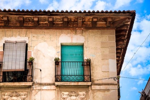 Old house facade with rusty balcony and wooden green blind. Novelda village, Valencia community, Spain.