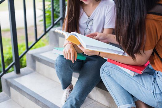 Close up of two Asian beauty girls reading and tutoring books for final examination together. Student smiling and sitting on stair. Education and Back to school concept. Lifestyles and People theme.