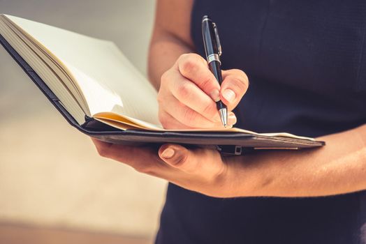 Closeup of young woman writing down letters in notepad for making note at her diary with her hand. Business and Lifestyle concept. People and Accountant concept. Working woman theme. Warm bright tone