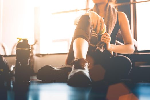 Sport woman sitting and resting after workout or exercise in fitness gym with protein shake or drinking water on floor. Relax concept. Strength training and Body build up theme. Warm and cool tone 