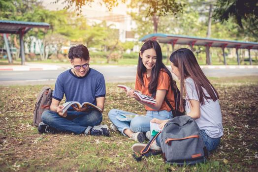 Group of Asian college student reading books and tutoring special class for exam on grass field at outdoors. Happiness and Education learning concept. Back to school concept. Teen and people theme.