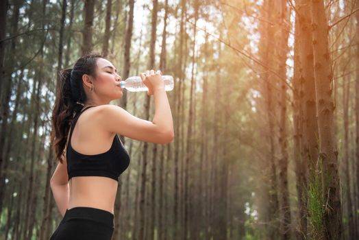 Asian beauty woman drinking water in forest. Sport and Healthy concept. Jogging and Running concept. Relax and take a break theme. Outdoors activity theme.