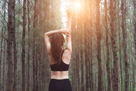 Women stretching arms and breathing fresh air in middle of pinewood forest while exercising. Workouts and Lifestyles concept. Happy life and Healthcare theme. Nature and Outdoors theme. Back view