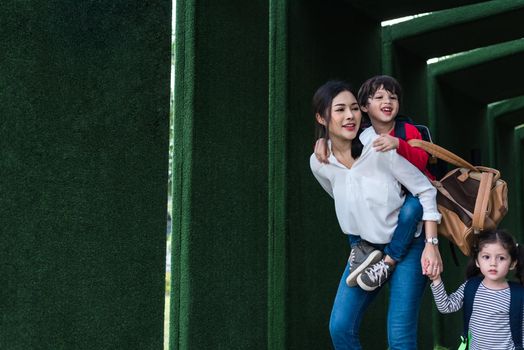 Single mom carrying and playing with her children in garden with green wall background. People and Lifestyles concept. Happy family and Home sweet home theme. Outdoors and nature theme.