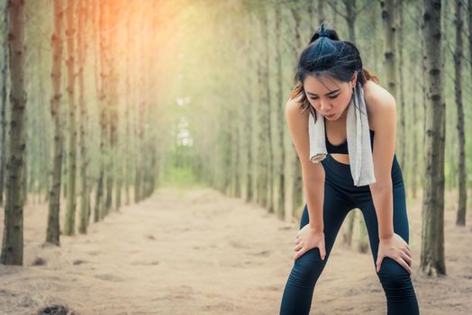 Asian beauty woman tiring from jogging in forest. Towel and sweat elements. Sport and Healthy concept. Jogging and Running concept. Relax and take a break theme. Outdoors activity theme.