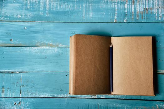Top view of blank open notebook on blue wooden background with purple pencil in middle. Working stationery office. Education and Business concept. Minimal and Flat lay theme. Copy space on left