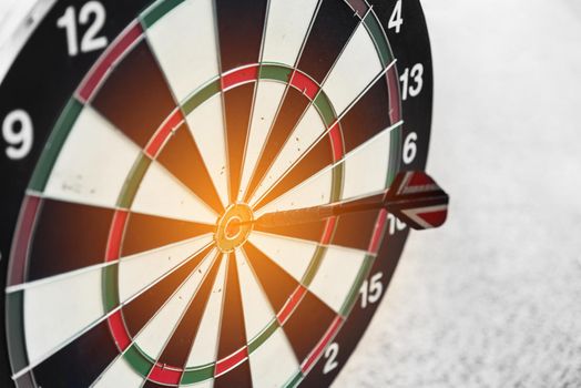 Dart board and arrow in middle. Business and success concept. Achievement and target theme. Orange sun light effect. High contrast tone
