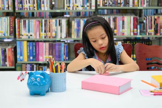 Asian girl folding and crafting paper in library during art class. Education and activity concept