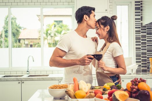 Asian lovers or couples kissing forehead and drinking wine in kitchen room at home. Love and happiness concept Sweet honeymoon and Valentine day theme