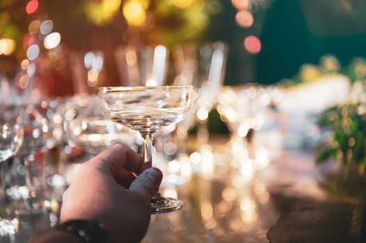 Closeup hand holding martini wine glasses on outdoors counter bar in the garden at night for celebration party.