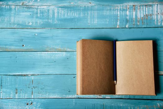 Top view of blank open notebook on blue wooden background with purple pencil in middle. Working stationery office. Education and Business concept. Minimal and Flat lay theme. Copy space on left