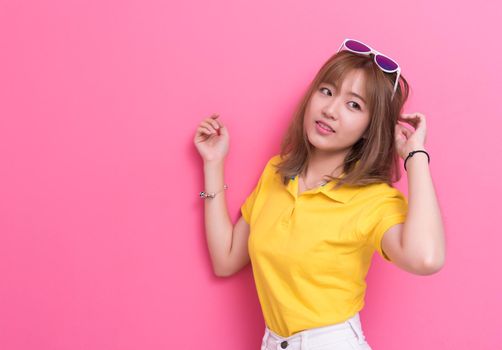 Beauty woman posing with sunglasses in front of pink wall background. Summer and vintage concept. Happiness lifestyle and people portrait theme. Cute and pastel tone.
