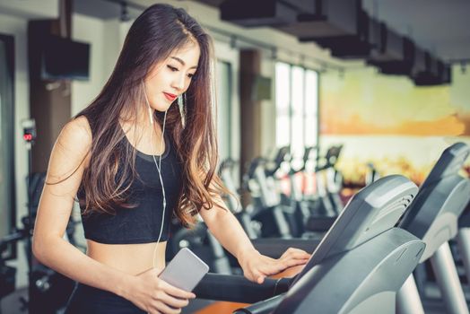 Asian woman using smart phone when workout or strength training at fitness gym on treadmill. Relax and Technology concept. Sports Exercise and Health care theme. Happy and Comfortable mood.