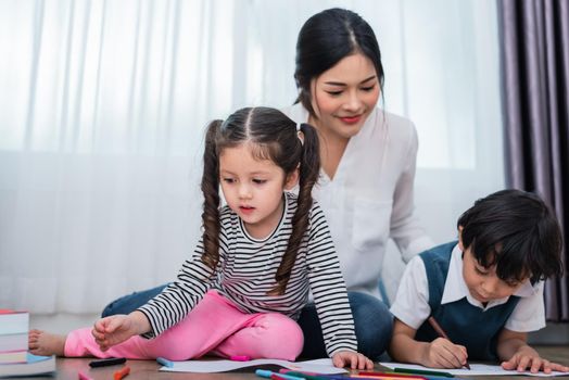 Mother teaching children in drawing class. Daughter and son painting with colorful crayon color in home. Teacher training students in art classroom. Education and Learning development of kids theme.