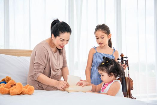 Asian mother teaching mixed raced girls daughter to reading books in their house. Quarantine in home concept. Happy family theme.