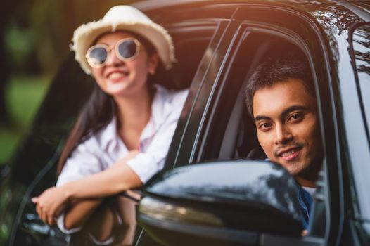 Happy Asian man looking outside open window car with his girlfriend on forest background. People lifestyle relax as traveler on road trip in holiday vacation. Transportation travel. Looking at camera
