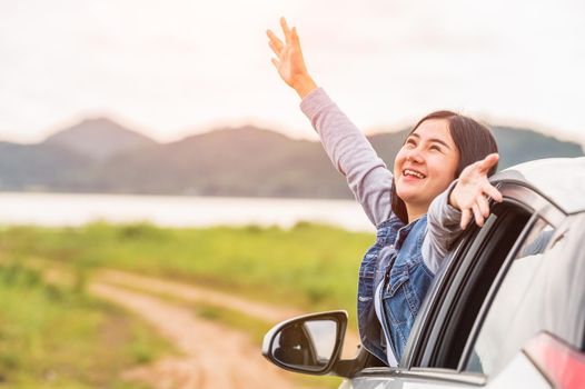 Happy Asian woman spread arms out of window under sunset at seaside with nature  background during travel in holiday. Confidence cheerful girl with dawn sky. Sun sea and mountain. Vacation concept