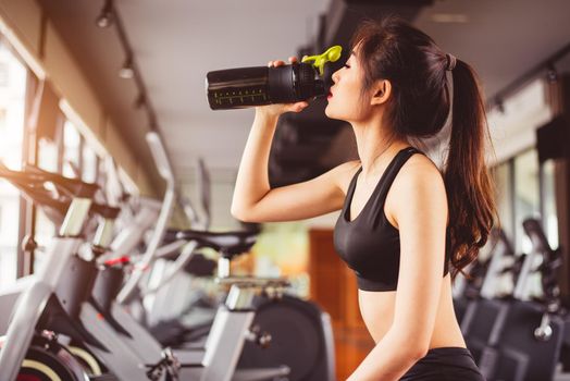 Asian beautiful woman drinking protein shake or drinking water in sport fitness training gym. Sports and people concept. Fitness and workout theme. Girl having activity on condominium or apartment